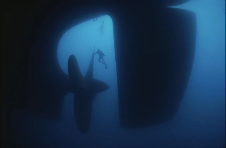 Diver touching a big ship propeller underwater. Submechanophobia.